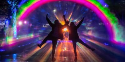 Two people in silhouette with their arms and legs outstretched, in front of a bright rainbow light